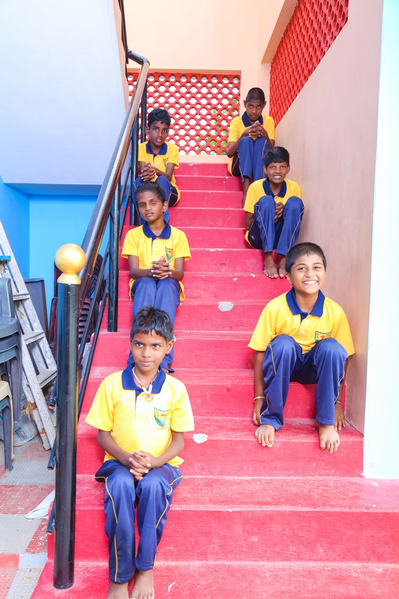 Children in Synthika Trust uniforms sitting on the stairs of the home